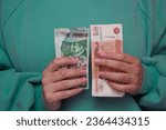 Woman in green long sleeved sweater holds stack of paper money. Russian banknote 5000 rubles and Georgian bill 50 lari in female hand. Cash in Georgia and Russia for tourism, travel, payments, salary