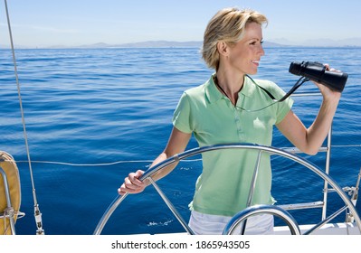 Woman In Green Polo Shirt Standing With Binoculars At The Helm Of Sailing Boat Out At Sea.