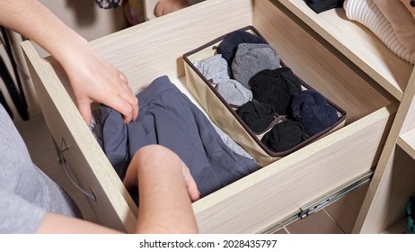 Woman in grey t-shirt hands choose rolled socks in open drawer of large wooden cabinet in contemporary walk-in closet at home close view