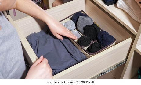 Woman in grey t-shirt hands choose rolled socks in open drawer of large wooden cabinet in contemporary walk-in closet at home close view
