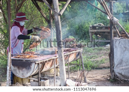 Woman grilled chicken on the street food in countryside of Thailand.
Grilled Chicken on a Stove with Smoke.Grilled chicken causes cancer.