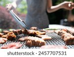 Woman grilling meat using tongs on barbecue