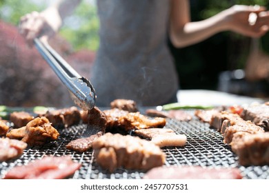 Woman grilling meat using tongs on barbecue - Powered by Shutterstock