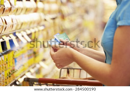 Woman In Grocery Aisle Of Supermarket With Coupons