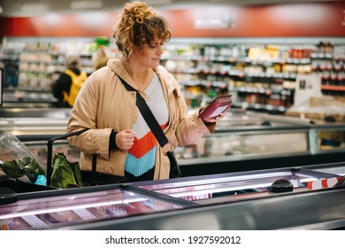 Woman At Grocery Store Reading Product Information On Food Products. Female Customer Looking At Label Of A Food Item At Grocery Store.