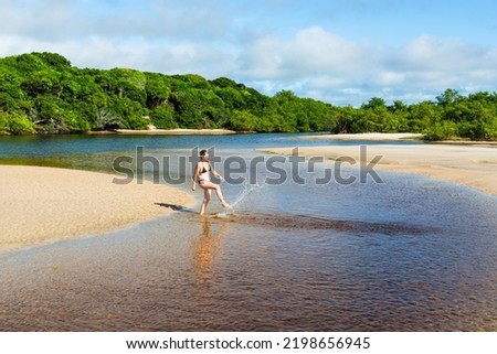 A woman, in the Guaibimzinho River, kicks water into the air. Praia do Guaibim, coast of the sea of Bahia, Brazil
