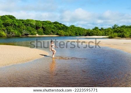 A woman, in the Guaibimzinho River, kicks water into the air. Praia do Guaibim, coast of the sea of Bahia, Brazil