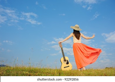 Woman And Guitar Standing On Meadow With Cloud Sky