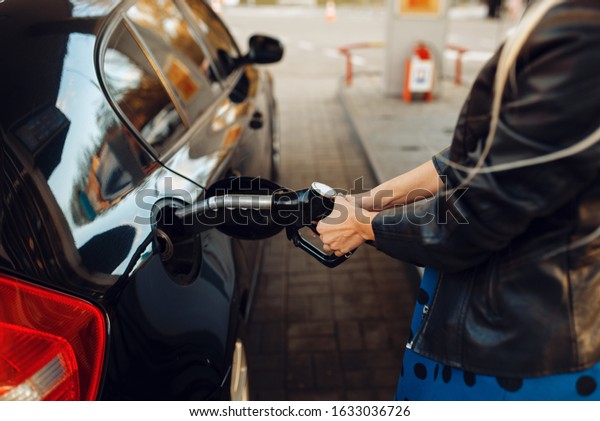Woman with gun\
fuels vehicle on gas\
station
