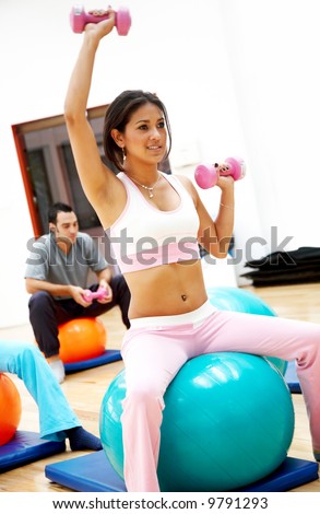 woman at the gym doing free weights sitting on a pilates ball