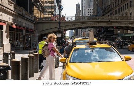 Woman hailing a yellow taxi on a busy street by Grand Central Terminal with American flags in the background - Powered by Shutterstock