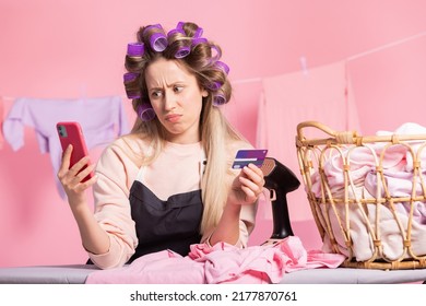 A Woman With Hair Rollers On Her Head Does Housekeeping Irons Clothes Hangs Laundry On A String. Girl Orders Cleaning Products On Phone, Purchases Pay With Bank Card Using App.