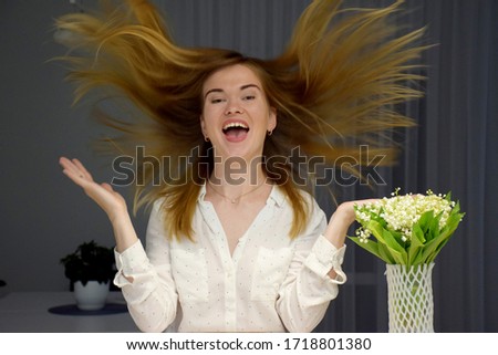 Woman with hair stand on end in white shirt near bouquet of flowers lilies of the valley