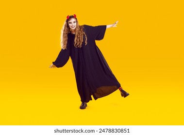 Woman in Halloween costume moving, dancing, rocking and having fun. Full length shot of happy young girl wearing long black robe and devil horns dancing isolated on yellow color background - Powered by Shutterstock