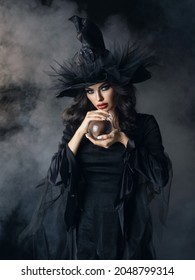 Woman In Halloween Witch Costume With Crystal Ball. Beautiful Sexy Model Girl In Sinister Costume And Make Up