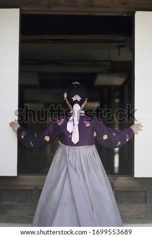 Woman in Hanbok standing at traditional Korean house