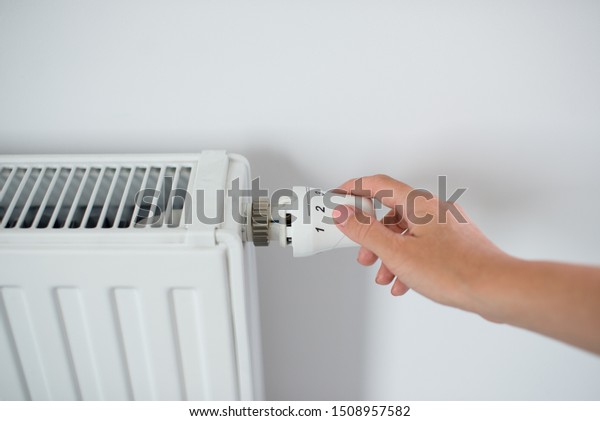 Woman Hand Adjusting The\
Knob Of Heating Radiator. The valve from the radiator - Heating.\
Hand adjusting thermostat valve of heating radiator in a room. Copy\
space.