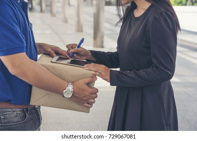 woman hand appending receive sign signature after accepting a delivery of boxes from delivery man in blue uniform holding package, sign and receive delivery concept