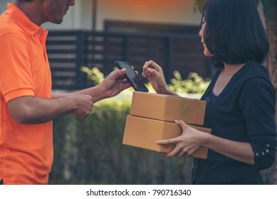 Woman hand appending receive sign signature after accepting a delivery of boxes from delivery man in blue uniform holding package, sign and receive delivery concept