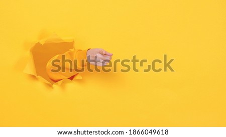 Woman hand arm pointing finger camera isolated through torn yellow wall orange background studio Copy space advertisement place for text or image promotional content Advertising area workspace mock up