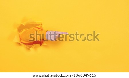 Woman hand arm pointing on copyspace isolated through torn yellow wall orange background studio. Copy space advertisement place for text or image promotional content Advertising area workspace mock up