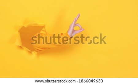 Woman hand arm showing ok okay gesture isolated through torn yellow wall orange background studio. Copy space advertisement place for text image promotional content Advertising area workspace mock up