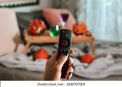 Woman Hand With Black Manicure Holding Tv Remote With Halloween Decor In Background, Halloween Movie Night Concept