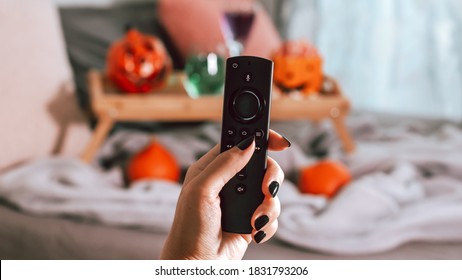 Woman Hand With Black Manicure Holding Tv Remote With Halloween Decor In Background, Halloween Movie Night Concept
