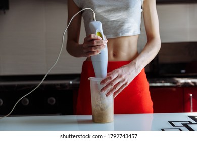 Woman With Hand Blender Making Sweet Banana Protein Powder Milkshake Smoothie. Protein Shake After Workout. Sport Nutrition Diet After Gym. Healthy Lifestyle