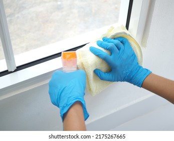 Woman hand in blue gloves cleaning dust on the glass window rail with cream rag and spray detergent. Housework concept. closeup photo, blurred.
