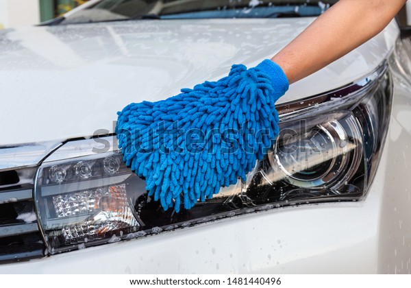 Woman hand with\
blue microfiber fabric washing headlight modern car or cleaning\
automobile. Car wash\
concept