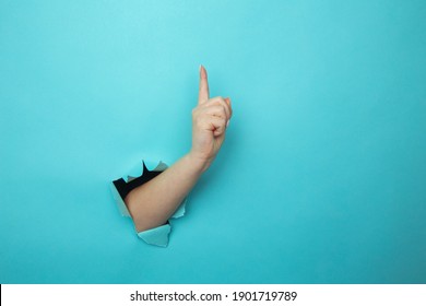 Woman hand breaking through blue paper wall with finger point up