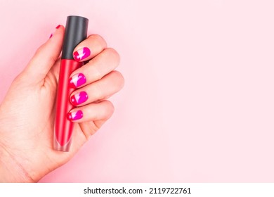 Woman hand and bright manicure holding red lip gloss isolated pink background 