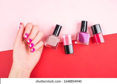 Woman hand and bright manicure   nail polish bottles isolated red   pink background 