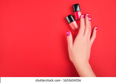 Woman hand and bright manicure   nail polish bottles isolated red background 