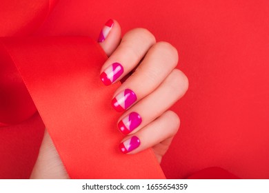 Woman hand and bright manicure   shiny red ribbon isolated red background 