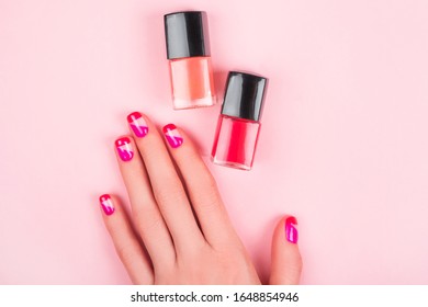 Woman hand and bright manicure   two nail polish bottles isolated pink background 