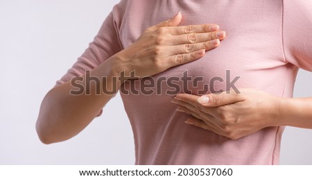 Woman hand checking lumps on her breast for signs of breast cancer on gray background. Healthcare concept.