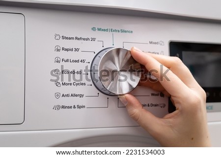 Woman hand choosing program on automatic washing machine for daily laundry at home. Turning knob on control panel for anti allegry washing, close up Stock photo © 