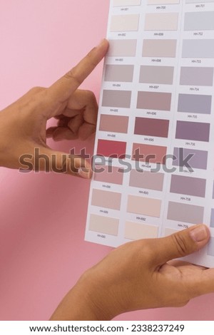 Woman hand choosing rosy or pink painting color in sample palettes. Close-up