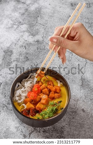Woman hand with chopsticks holding piece of Poke Bowl or Asian udon noodles with vegetables on grey background.  copy space. Minimalist style 
