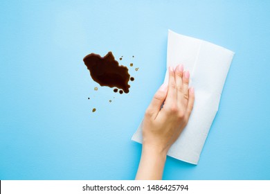 Woman hand cleaning fresh spilled dark beverage from pastel blue desk. Coffee stain simple removing with white paper napkin. Cleanup. Close up.  - Powered by Shutterstock