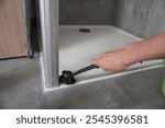 woman hand cleaning shower door frame with brush on tiled bathroom floor. 