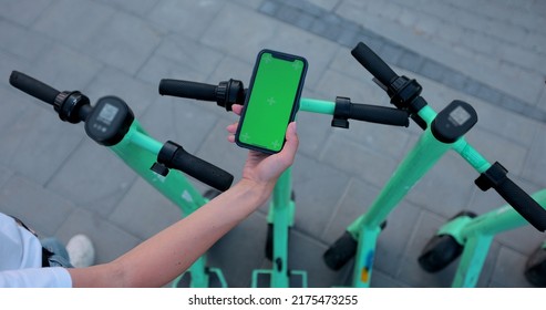 Woman Hand Click Phone With Chromakey On Background Of Electric Scooter In Public Park, Mockup, Chromakey. Urban Style Riding Ecological Transport.