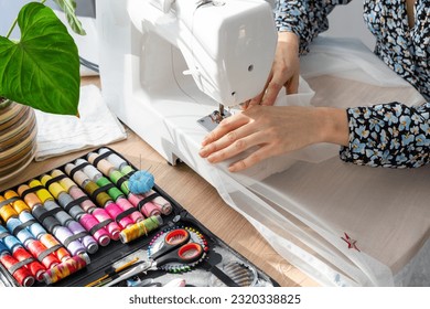 Woman hand close up sews tulle on electric sewing machine. Filling the thread into the sewing needle, adjusting the tension. Comfort in the house, a housewife's hobby, layout of sewing tools - Powered by Shutterstock