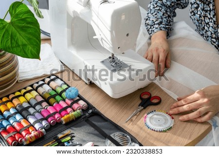 Woman hand close up sews tulle on electric sewing machine. Filling the thread into the sewing needle, adjusting the tension. Comfort in the house, a housewife's hobby, layout of sewing tools