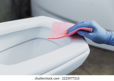 Woman Hand Closeup Gloved In Rubber Protective Gloves. Housewife Cleaning Toilet Bowl, Seat With Detergent, Pink Cloth In Bathroom Or Public Restroom. Disinfection, Hygiene, Cleaning Service Concept