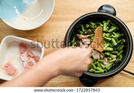 Woman hand cooking Thaifood with yardlong bean and pork meat on the wooden table top view angle