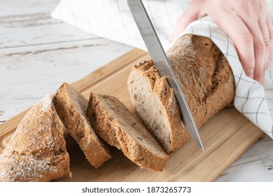 Woman hand cutting loaf of bread on white wooden table. Loaf of wholegrain bread