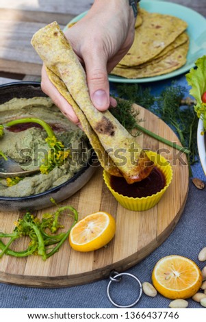 Woman hand dips roll of chapati or roti into red hot ketchup sauce. Whole wheat Indian flat bread with vegetables and greens